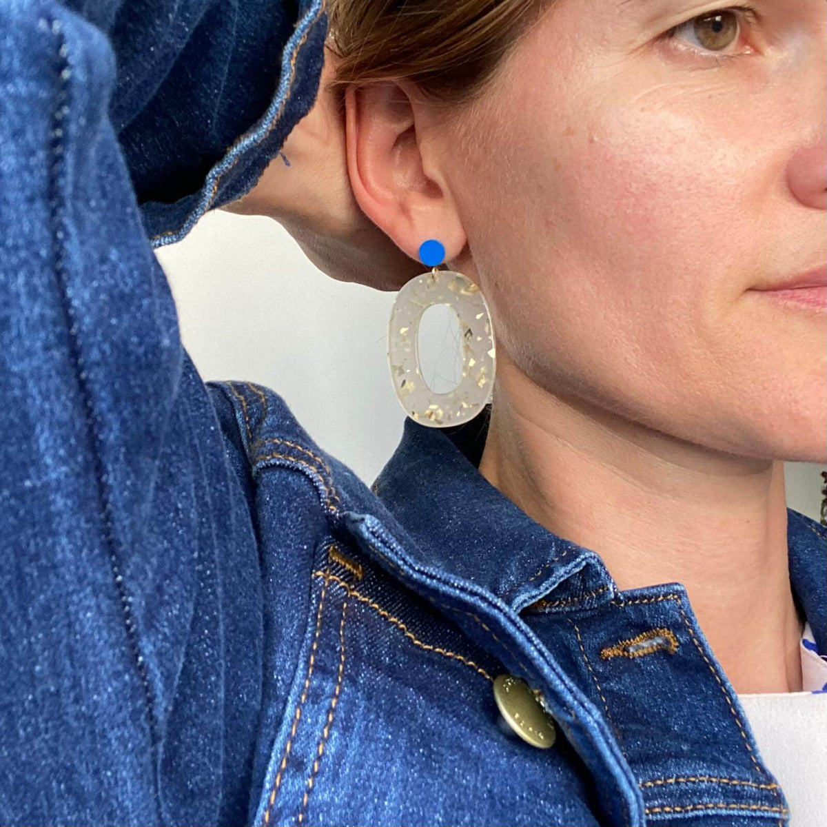 Boucles d'oreille paillettes or et Lego portées par une femme, avec un design élégant et coloré.