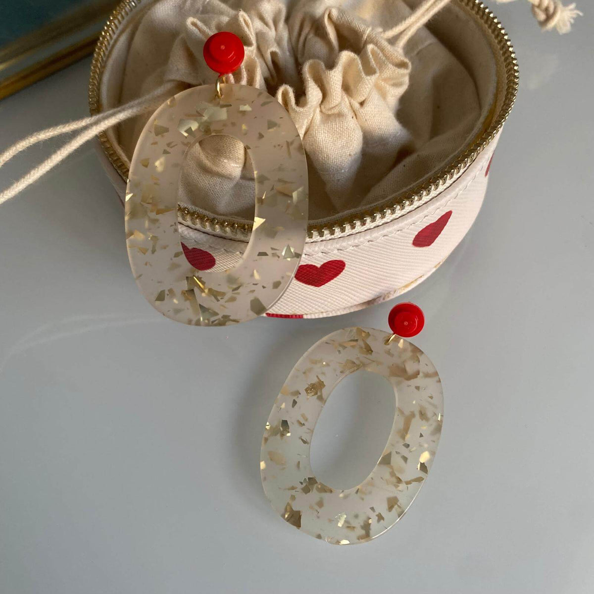 Boucles d'oreille paillettes or et Lego avec un pendentif ovale en acétate blanc et or et des détails en rouge.