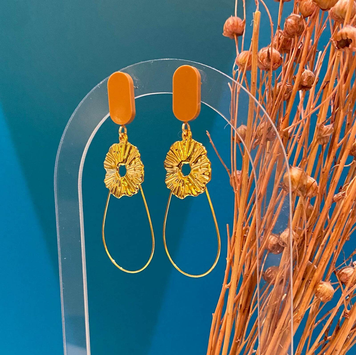 Boucles d'oreilles chic avec un Lego ovale et plat. En-dessous est suspendu une goutte en fil doré et un soleil. Le Lego apporte la touche de couleur à ce bijou fantaisie.