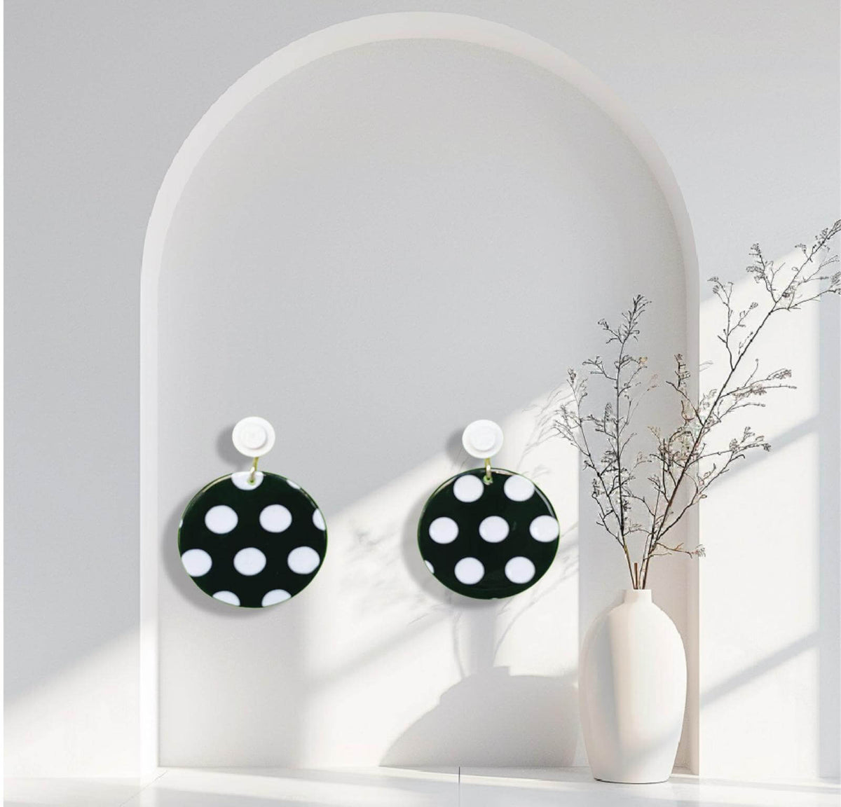 Boucles d'oreilles à pois noirs et blancs accrochées à l'oreille par une brique de Lego ronde dans un décors minimaliste