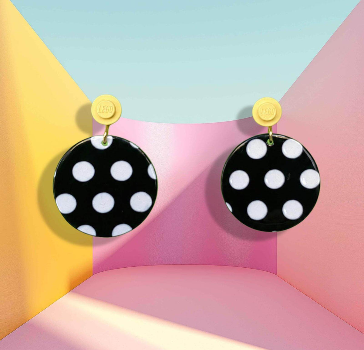 Boucles d'oreilles à pois noirs et blancs qui s'accrochent à l'oreille par une brique de Lego ronde jaune pastel dans un décor psychédélique kawaï