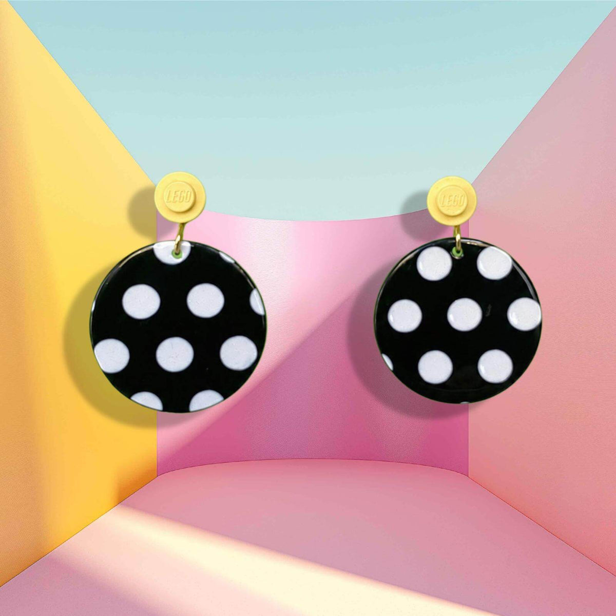 Boucles d'oreilles à pois noirs et blancs qui s'accrochent à l'oreille par une brique de Lego ronde jaune pastel dans un décor psychédélique kawaï