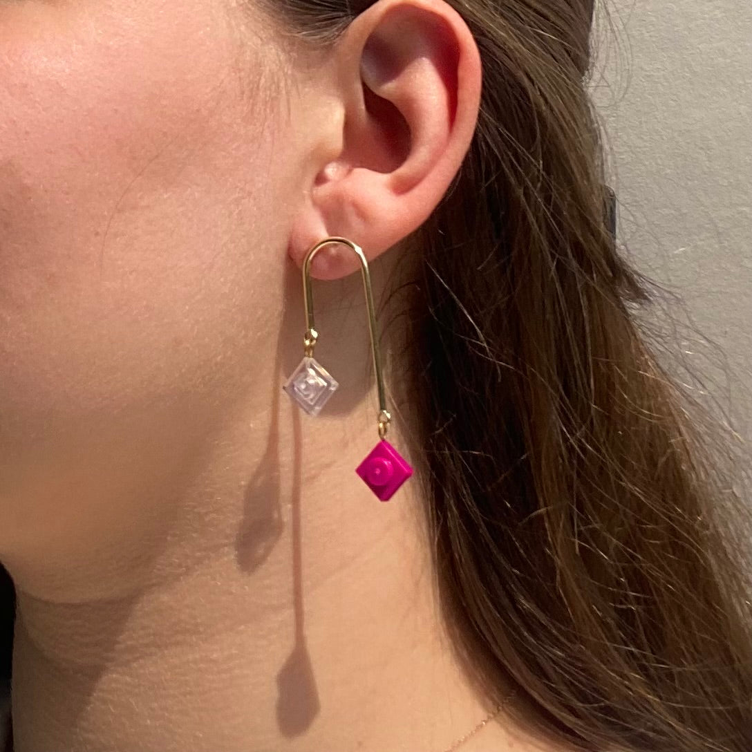 Boucles d'oreilles pendantes en or avec briques de Lego rose fuschia et transparente, style art déco, asymétriques et graphiques.