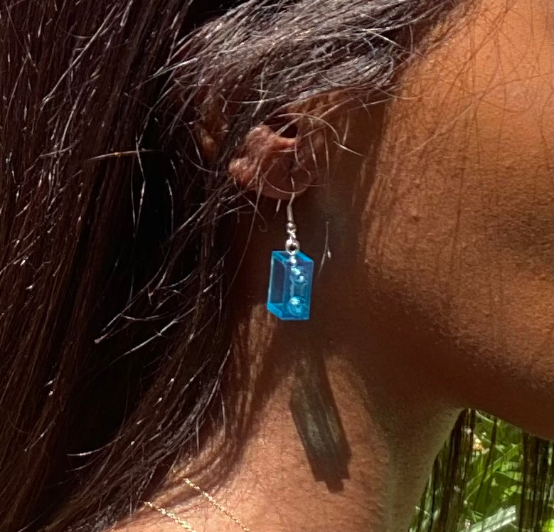 Boucles d'oreilles pendantes en brique Lego® bleue, élégamment portées, ajoutant une touche de couleur à votre look.