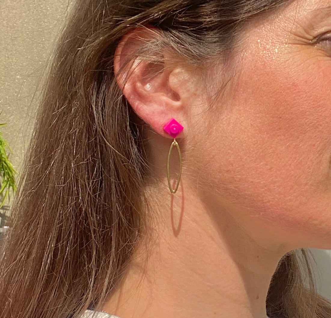Boucle d'oreilles pendante avec un ovale en laiton doré suspendue à une brique de Lego 1x1 plate rose pivoine ou fuschia. Elle se coordonne parfaitement avec un style rose, une tenue violette à la mode.