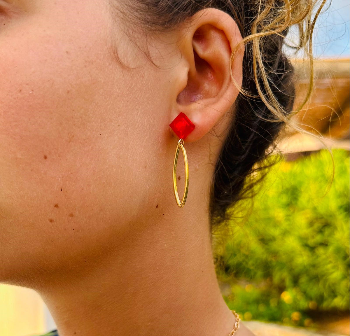 Boucle d'oreilles pendante avec un ovale en laiton doré suspendue à une brique de Lego 1x1 plate rouge transparente. Elle se coordonne parfaitement avec une tenue rouge ou noire.