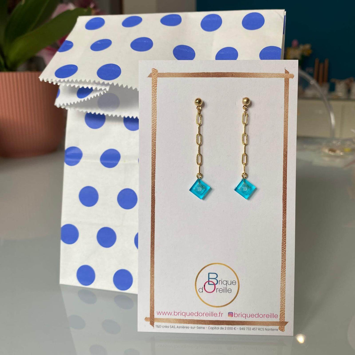 Boucles d'oreilles Lego® pendantes colorées avec chaine dorée avec un emballage assorti à pois bleus.
