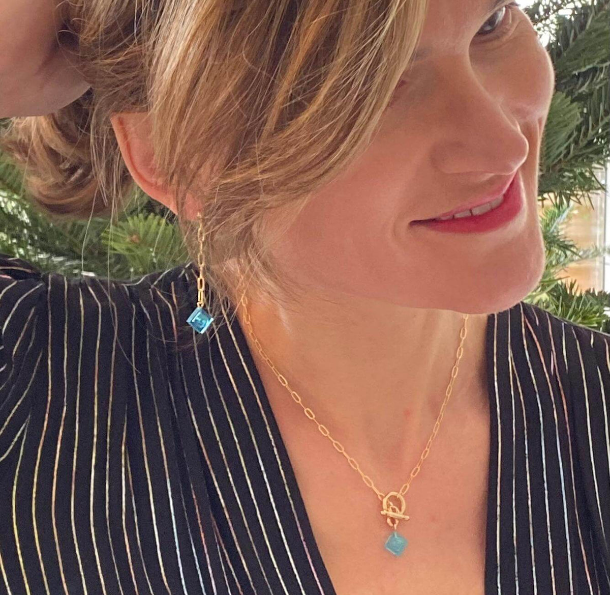 Femme portant des boucles d'oreilles pendantes dorées avec briques Lego colorées, look élégant et original.