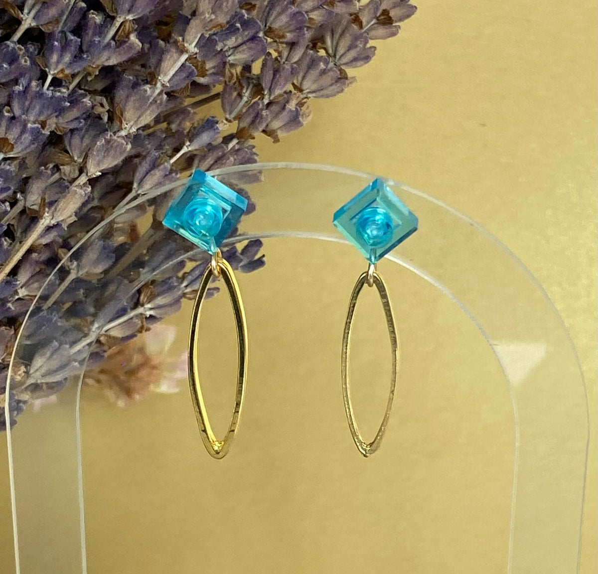 Boucle d'oreilles pendante avec un ovale en laiton doré suspendue à une brique de Lego 1x1 plate bleu clair transparent, effet pierre précieuse aigue-marine. Elle matche parfaitement avec votre look bleu, une tenue imprimée avec du bleu