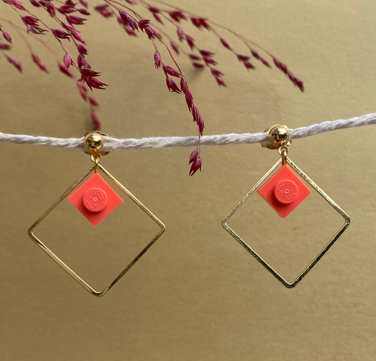 Boucles d'oreilles pendantes colorées avec un Lego corail inscrit dans un carré or