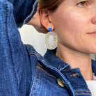Boucles d'oreille paillettes or et Lego portées par une femme, avec un design élégant et coloré.