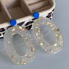 Boucles d'oreille paillettes or et Lego affichant des éléments en acétate blanc et des mini briques Lego colorées.
