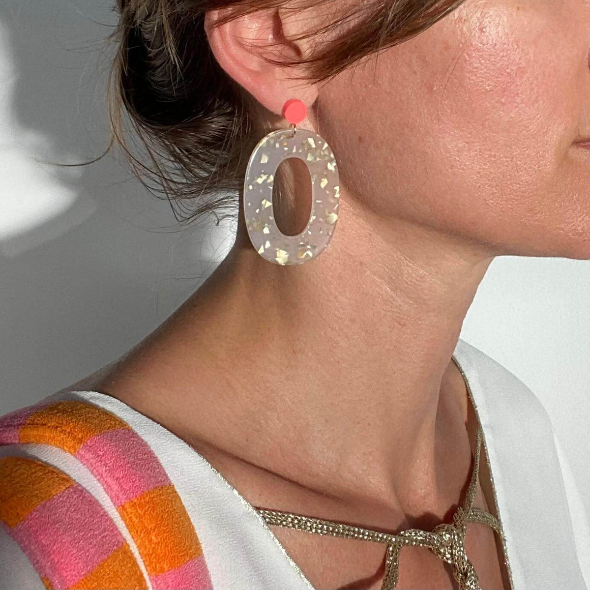 Boucles d'oreille paillettes or et Lego portées par une personne, avec pièce ovale en acétate et pastille Lego.