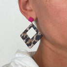 Boucles d'oreilles Léopard en acétate carré avec détail en rose portée par une personne.