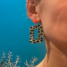 Boucles d'oreilles pendantes léopard et mini Lego portées, avec motif léopard et détail Lego rouge.