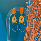 Boucles d'oreilles chic avec un Lego ovale et plat. En-dessous est suspendu une goutte en fil doré et un soleil. Le Lego apporte la touche de couleur à ce bijou fantaisie.