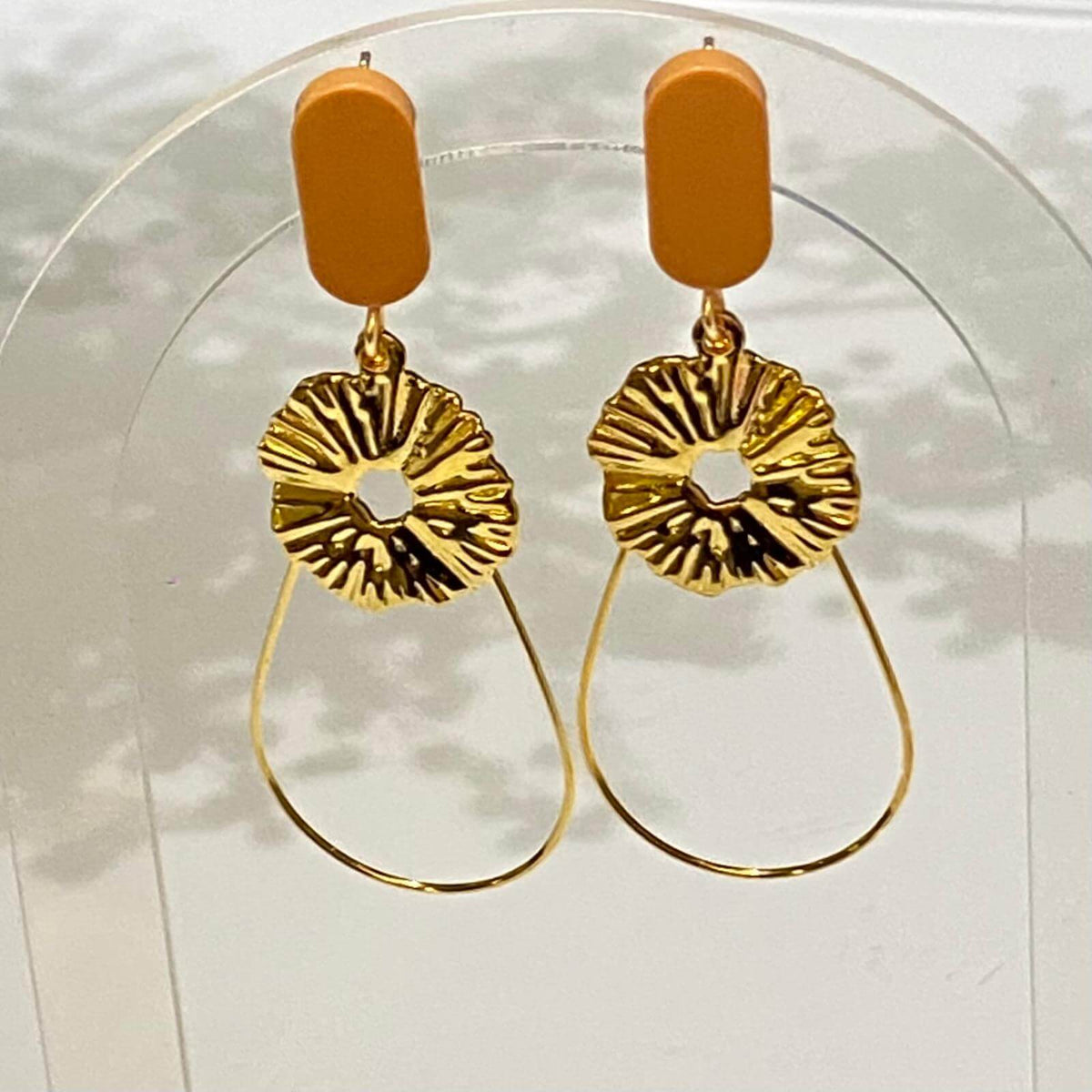 Boucles d'oreilles chic avec un Lego de forme ovale et plate, auquel est suspendu une fine goutte et une pièce dorée comme un soleil. Le Lego apporte la touche de couleur à ce bijou fantaisie.
