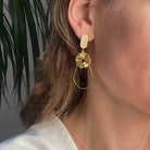 Boucles d'oreilles chic avec un Lego ovale et plat, sans tenon à l'oreille auquel est accroché une goutte en fil doré et un soleil. Un bijou délicat aux teintes make-up poudrées.