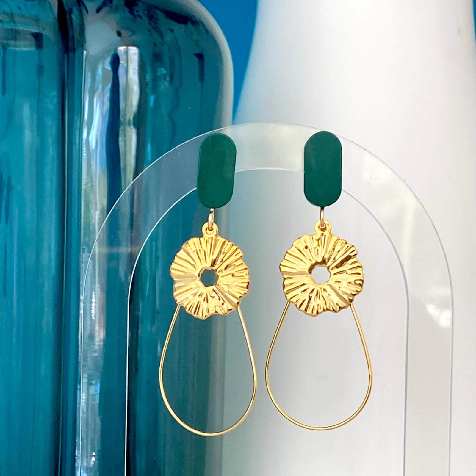 Boucles d'oreilles chic avec un Lego lisse et subtil auquel est suspendu une goutte en fil doré et un soleil. Un bijou avec un Lego vert foncé pour un effet ultra tendance