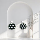 Boucles d'oreilles à pois noirs et blancs accrochées à l'oreille par une brique de Lego ronde dans un décors minimaliste