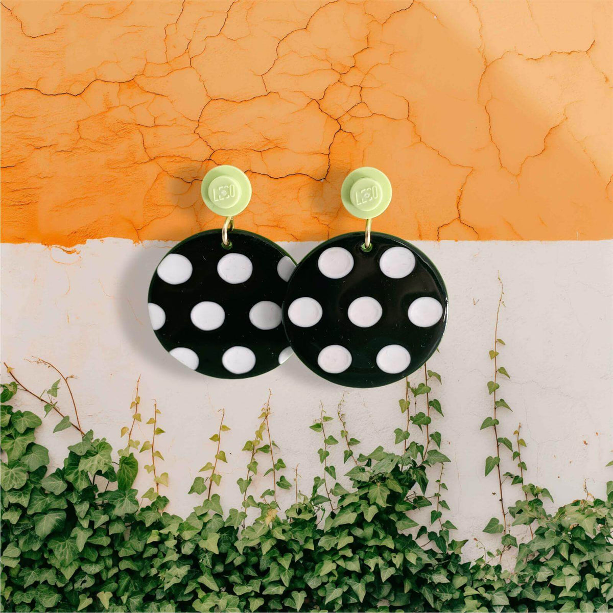 Boucles d'oreilles à pois noirs et blancs accrochées à l'oreille par une brique de Lego ronde vert citron vert 