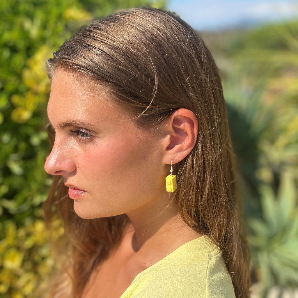 Boucles d'oreilles pendantes jaunes en brique Lego® portant par une femme au look décontracté en extérieur.