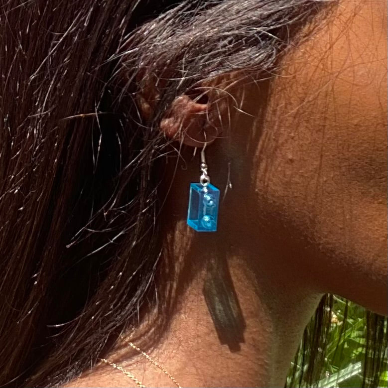 Boucles d'oreilles pendantes en brique Lego® bleue, élégamment portées, ajoutant une touche de couleur à votre look.
