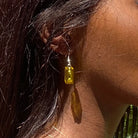 Boucles d'oreilles pendantes en brique Lego® jaune, ajoutant une touche colorée au look, portées avec des cheveux longs.