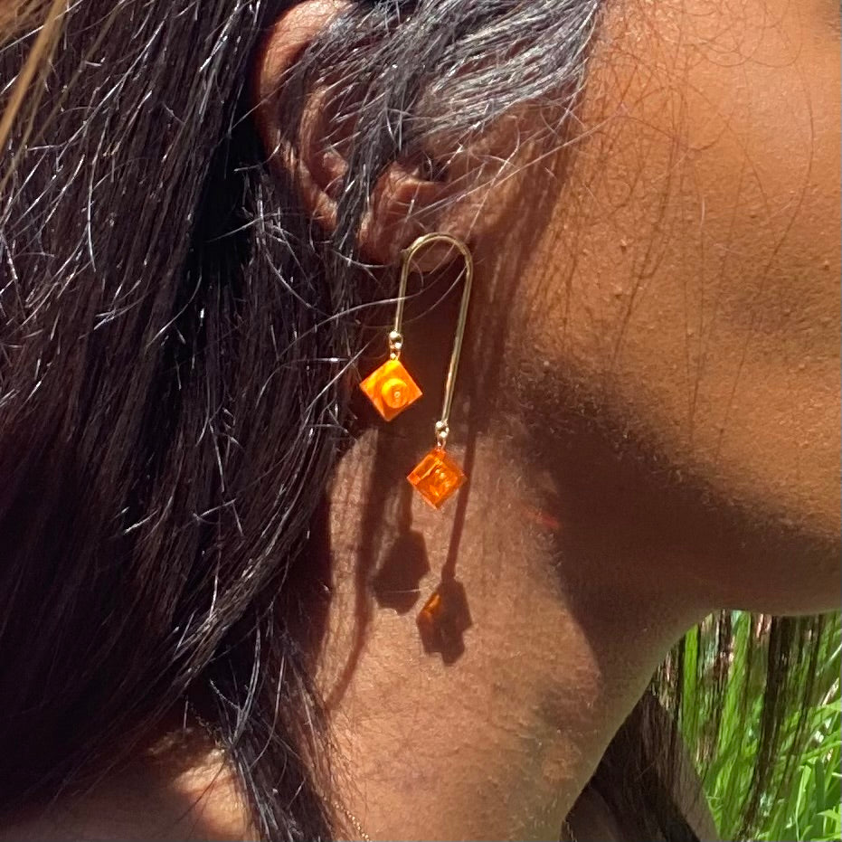 Boucles d'oreilles dorées pendantes asymétriques en petite brique de Lego orange, style art déco, ajout élégant à toute tenue.