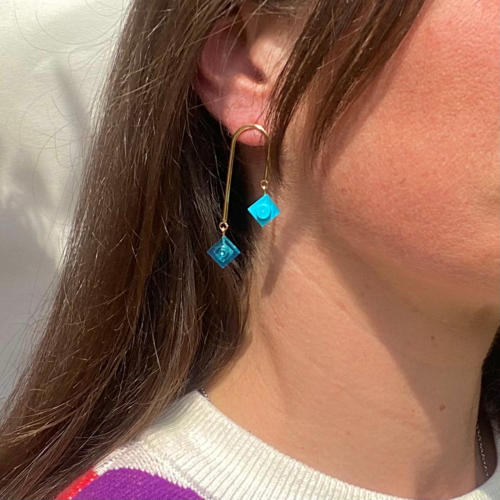 Boucles d'oreilles dorées pendantes asymétriques en style art déco avec briques LEGO colorées bleu turquoise, élégantes et graphiques.