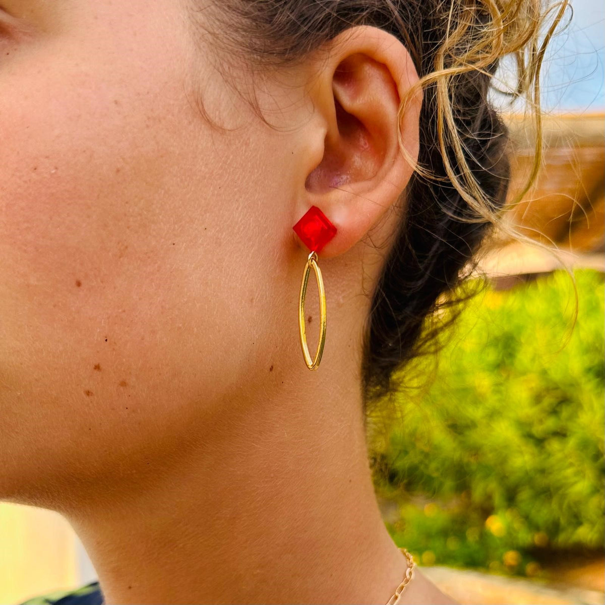 Boucle d'oreilles pendante avec un ovale en laiton doré suspendue à une brique de Lego 1x1 plate rouge transparente. Elle se coordonne parfaitement avec une tenue rouge ou noire.