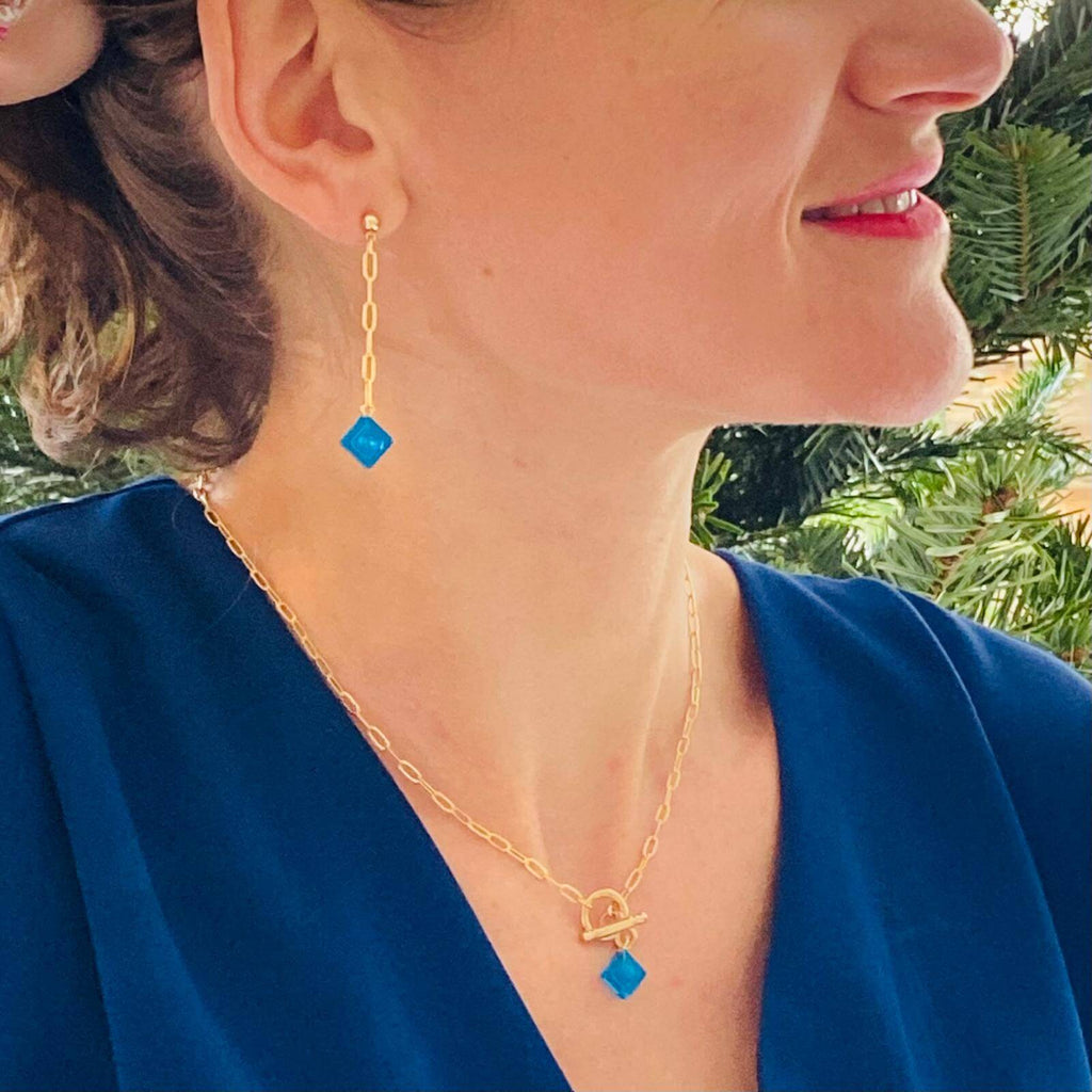Femme portant des boucles d'oreilles pendantes dorées avec un Lego bleu, accessoires élégants pour un look raffiné.