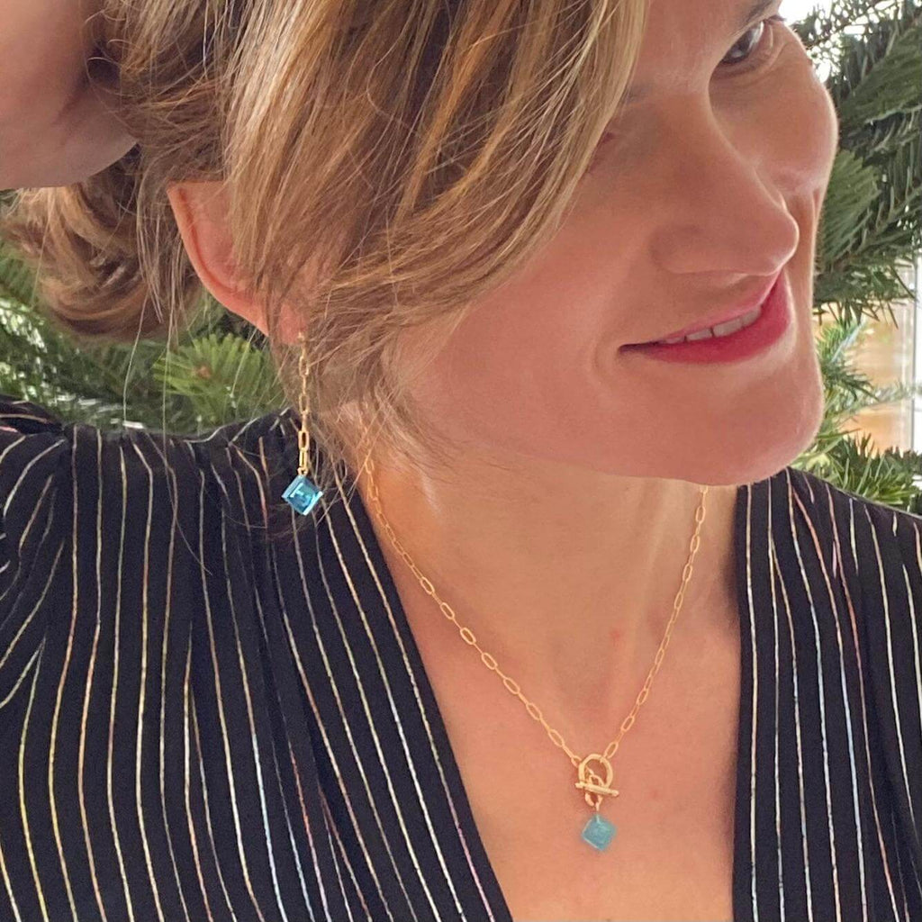 Femme portant des boucles d'oreilles pendantes dorées avec briques Lego colorées, look élégant et original.