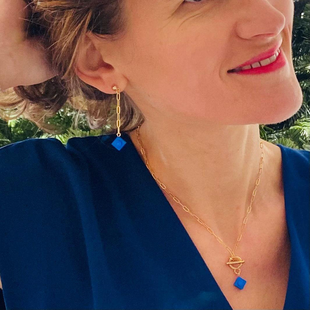 Boucles d'oreilles pendantes dorées avec brique Lego® bleue, portée avec un collier assorti, look élégant et fantaisie.