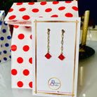 Boucles d'oreilles pendantes dorées avec briques Lego® rouge translucide effet rubis, présentées sur un support élégant.