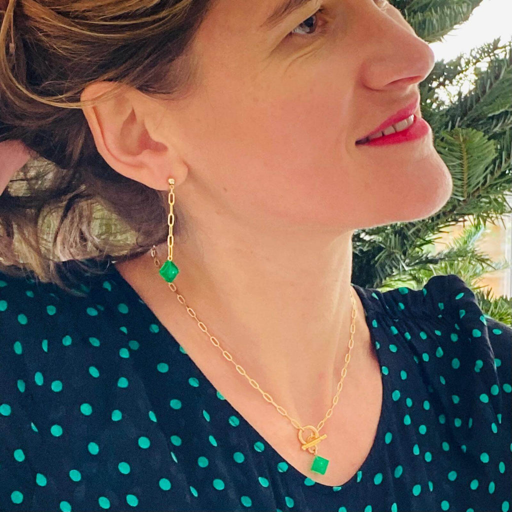 Femme portant des boucles d'oreilles pendantes dorées avec une brique Lego vert émeraude, mettant en valeur un look coloré et chic.
