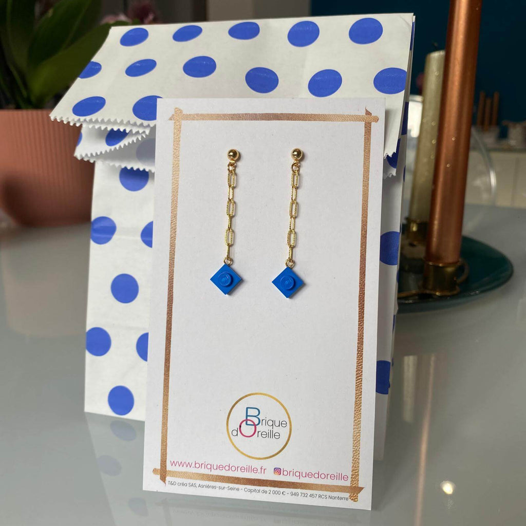 Boucles d'oreilles pendantes dorées en chaîne avec briques Lego® bleues, emballage cadeau assorti à pois.