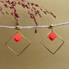 Boucles d'oreilles pendantes colorées avec un Lego corail inscrit dans un carré or