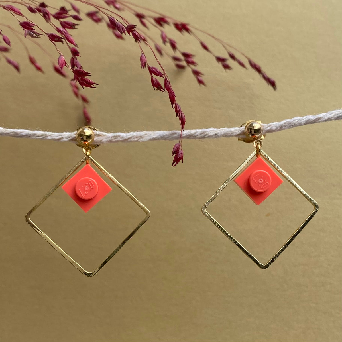 Boucles d'oreilles pendantes colorées avec un Lego corail inscrit dans un carré or